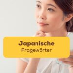 Asiatische Frau sitzt an einem Schreibtisch und hält mit einer Hand einen Notizblock und lernt japanische Fragewörter