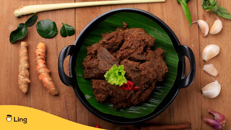 Auf einem Holztisch sind verschieden Kräuter und Gewürze dekoriert, on einem Teller ist Rind Rendang Pedang Curry einem traditionellen Gericht aus Malaysia