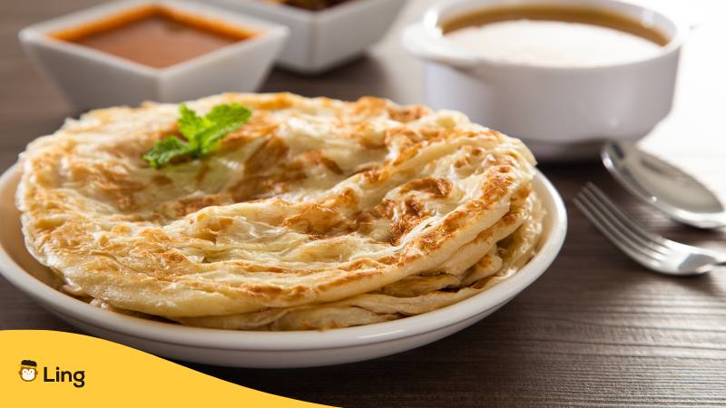 Malaysisches Gericht Roti Canai auf einem Teller mit kleinen Schüsseln mit Soße dahinter